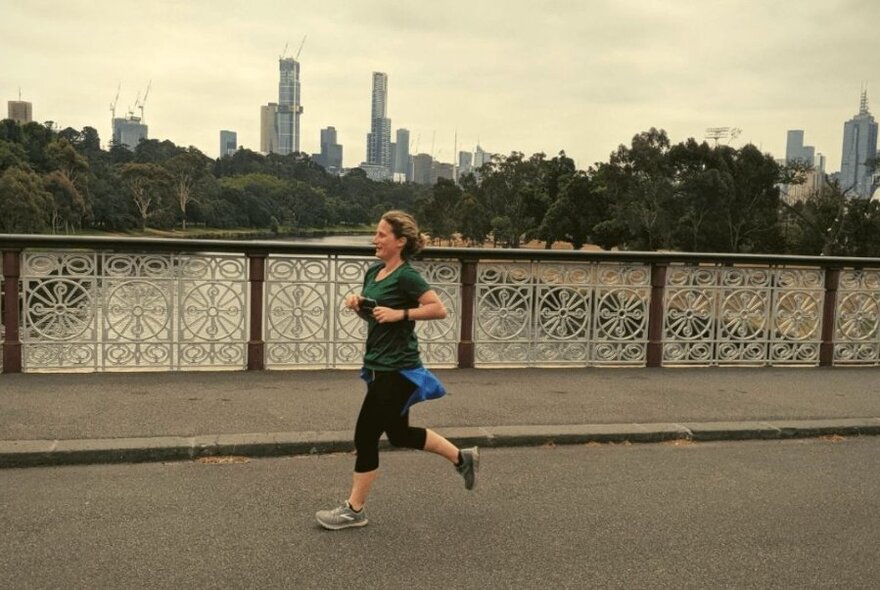 A jogger running across a bridge across the Yarra River with skyscrapers in the background.