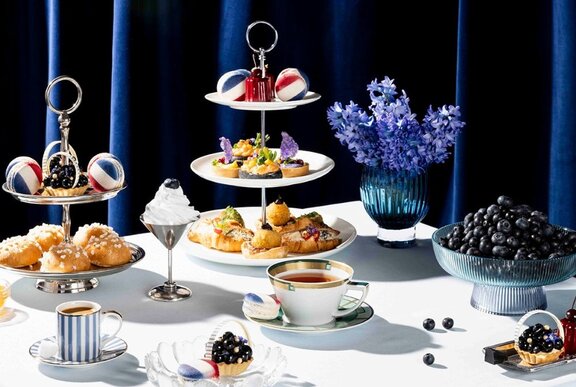 A table set for High Tea with a tiered cake platter, flowers and fruit.