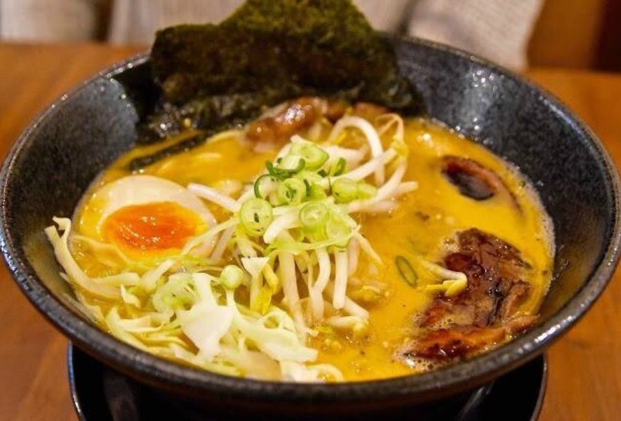 Ramen in a black bowl with egg, bean shoots and seaweed.