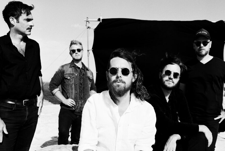 The five casually attired members of the musical band Boy & Bear posing for a group photo outdoors, some of them wearing dark sunglasses; black and white image.