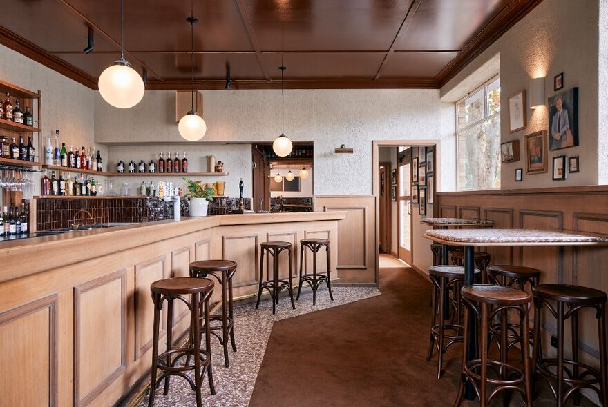 Interior of front room of a pub: wooden bar on left side, bar tables and stools to right.