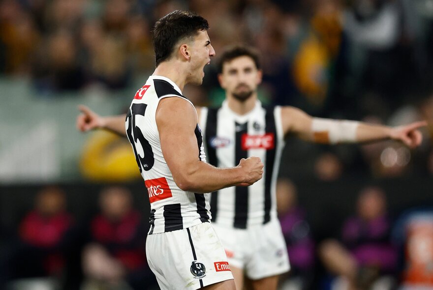 Collingwood player Nick Daicos celebrates a goal with his brother Josh blurred in the background. 