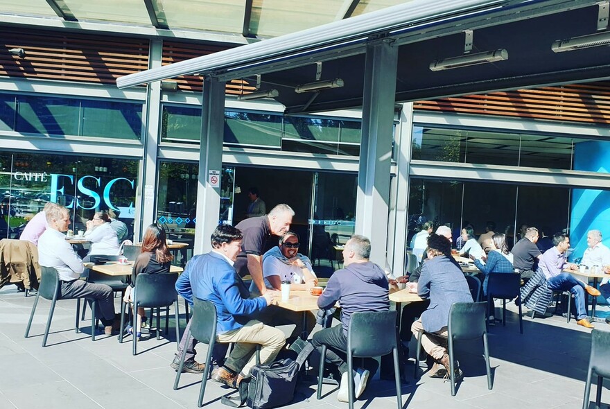 Cafe exterior with waiter serving a group of men at a table.