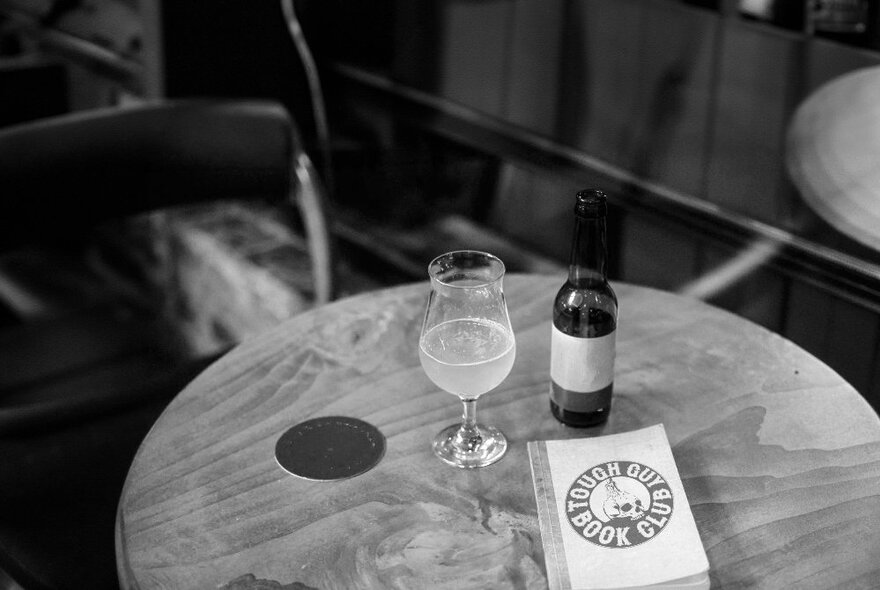 A black and white image of a table with a beer glass and bottle, and a book.