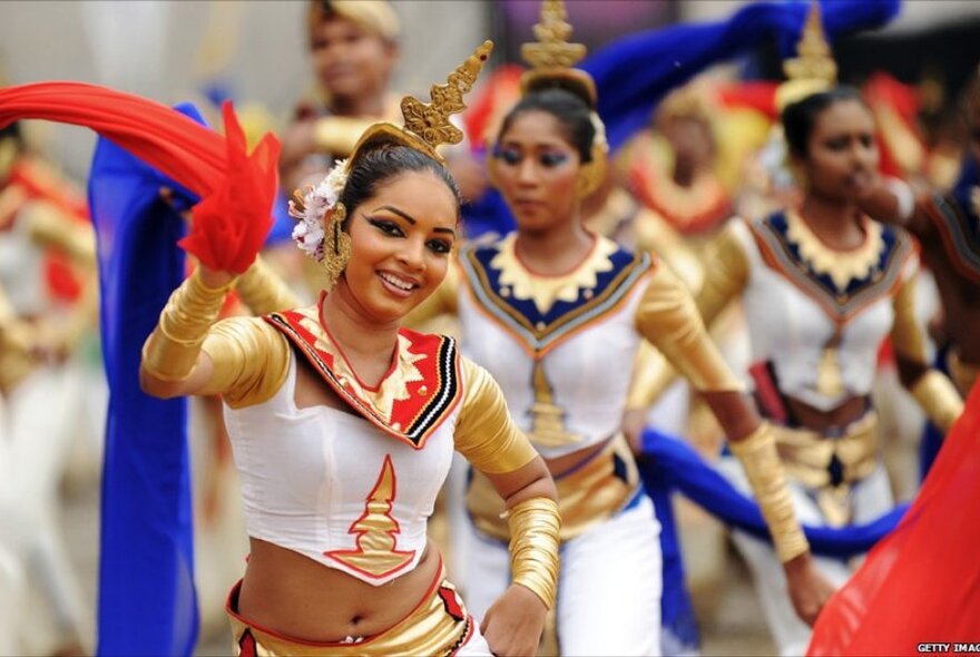 Women in elaborate Sri Lankan dress, dancing and the woman at the front is smiling. 