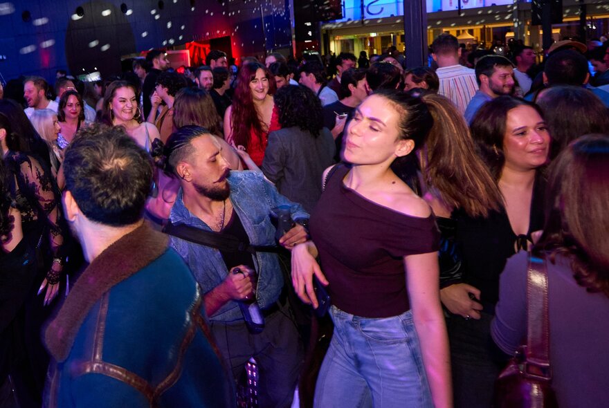 A crowded indoor dance floor with people dancing under disco-style lighting.