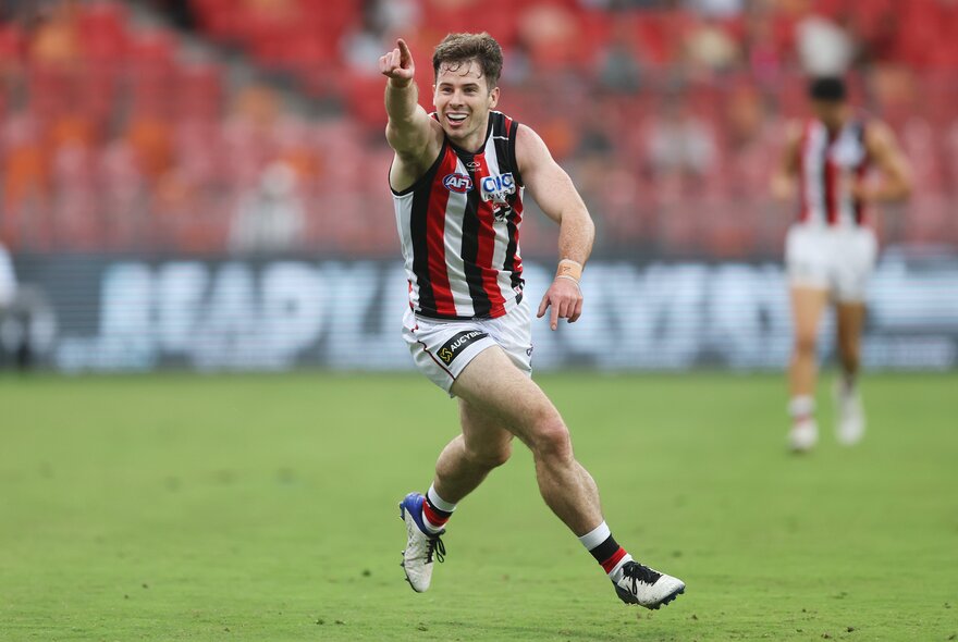 A St Kilda AFL football player running on the field during a match, with his arm pointing forward.