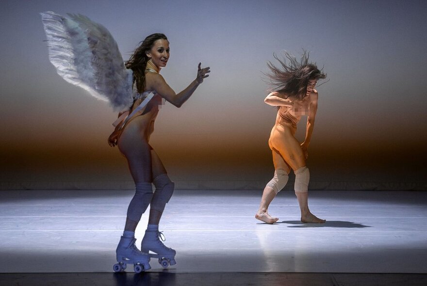 A woman on roller skates wearing wings, in front of a semi-naked dancing person.