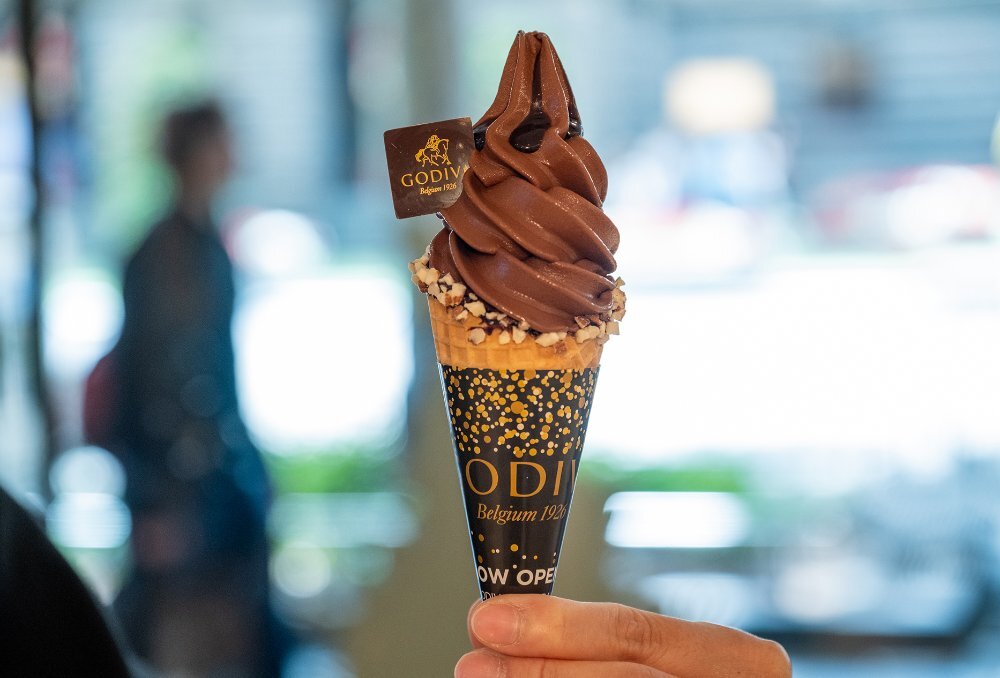 Someone holding up a chocolate ice cream in a cone.