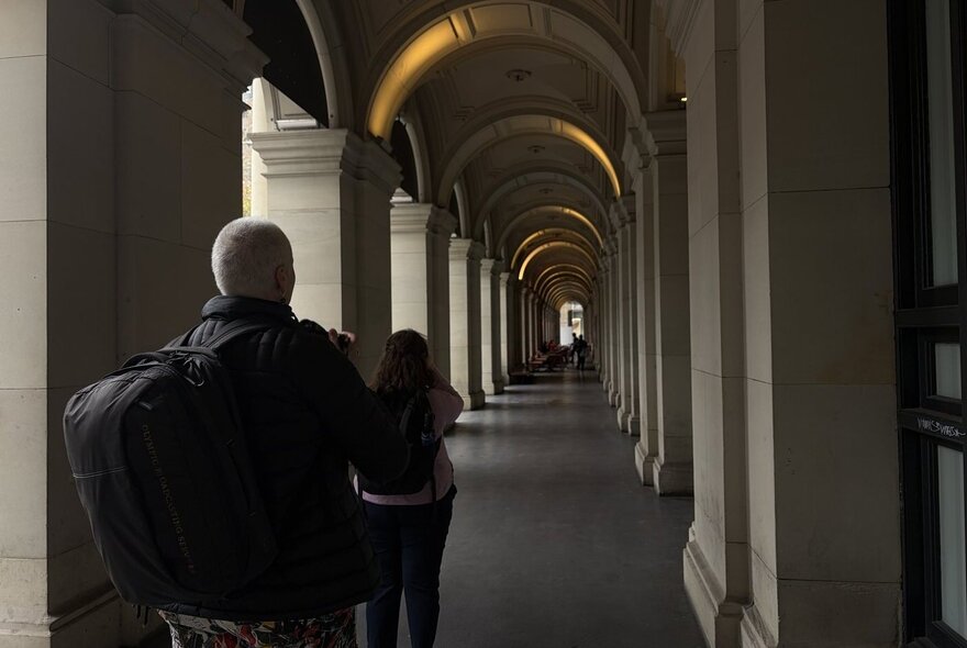 Dark silhouettes of people standing under arcaded passage with pillars and arches.