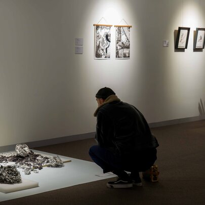 People in an exhibition space looking at exhibits, one person squatting to peer at a display of artefacts on the floor.