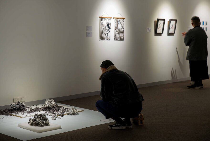 People in an exhibition space looking at exhibits, one person squatting to peer at a display of artefacts on the floor.