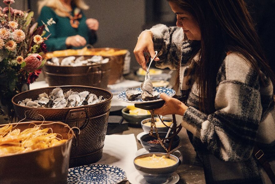 A view looking down a long table at a buffet, with small buckets of seafood and two people helping themselves. 