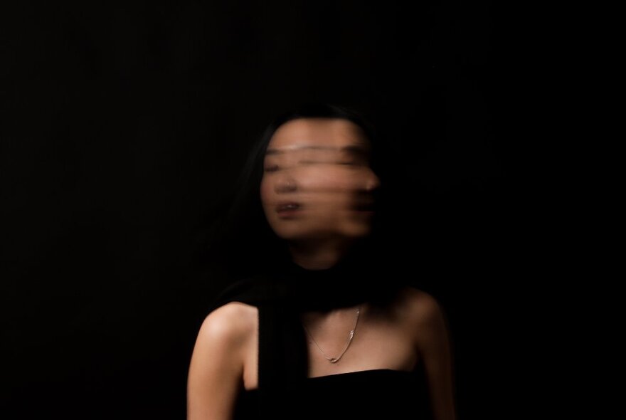 Blurred portrait of a person, as if in motion, against a black background.