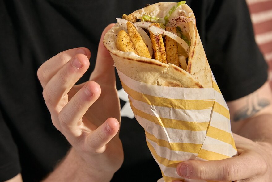 A hand holding a souvlaki wrap.