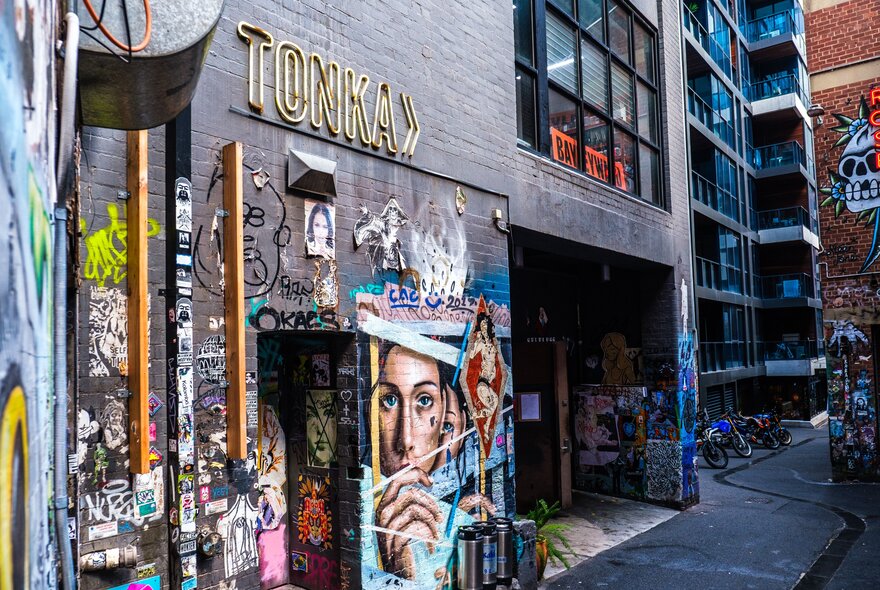A black brick wall in an alleyway with street art and a sign on it that says "Tonka".