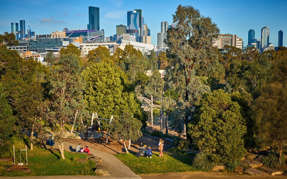 People enjoying a leafy park and playground next to the city.