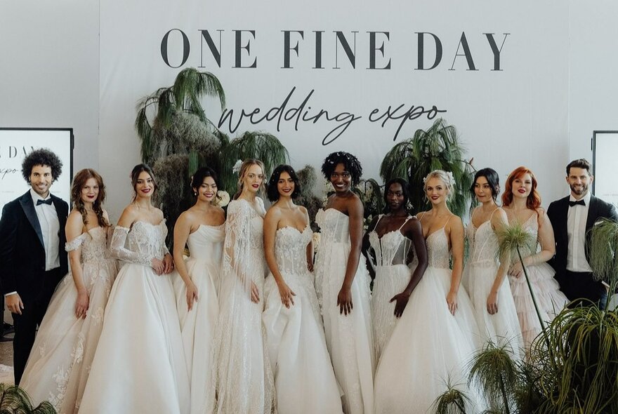 Fashion models wearing bridal dresses posed against a backdrop with the words ONE FINE DAY written in black on a white background.