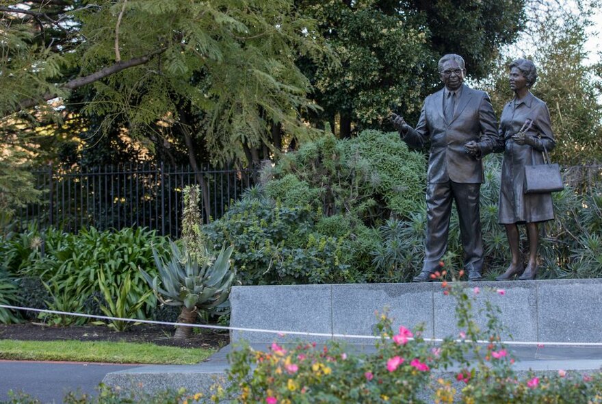 Bronze statue of Pastor Sir Douglas and Lady Gladys Nicholls Memorial surrounded by trees.