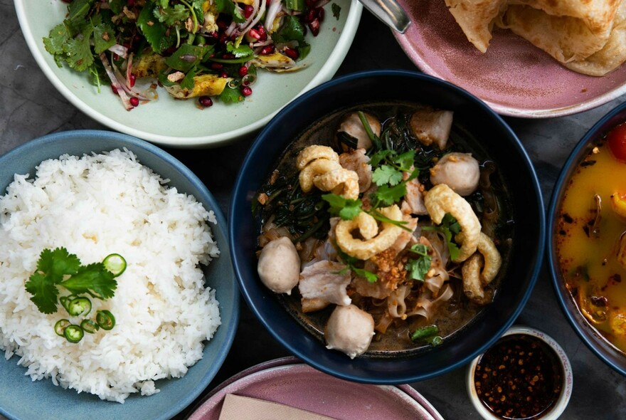 Several dishes crowded together including rice and Thai salads.