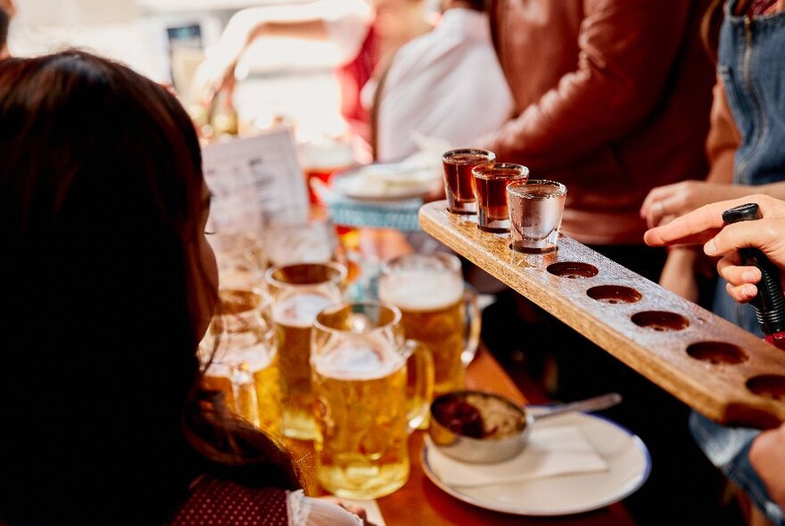 A flight of drinks at a table with many steins of beer.