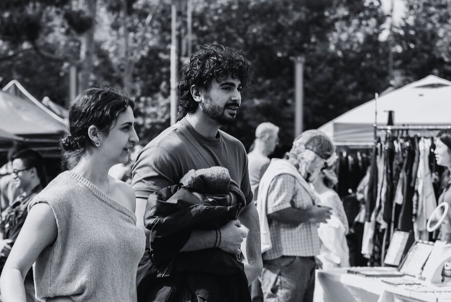 Black and white photograph of a young couple at an open air market, stalls in the background.