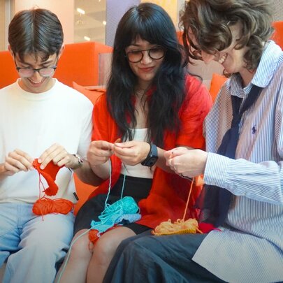 Three people crocheting together on orange chairs.