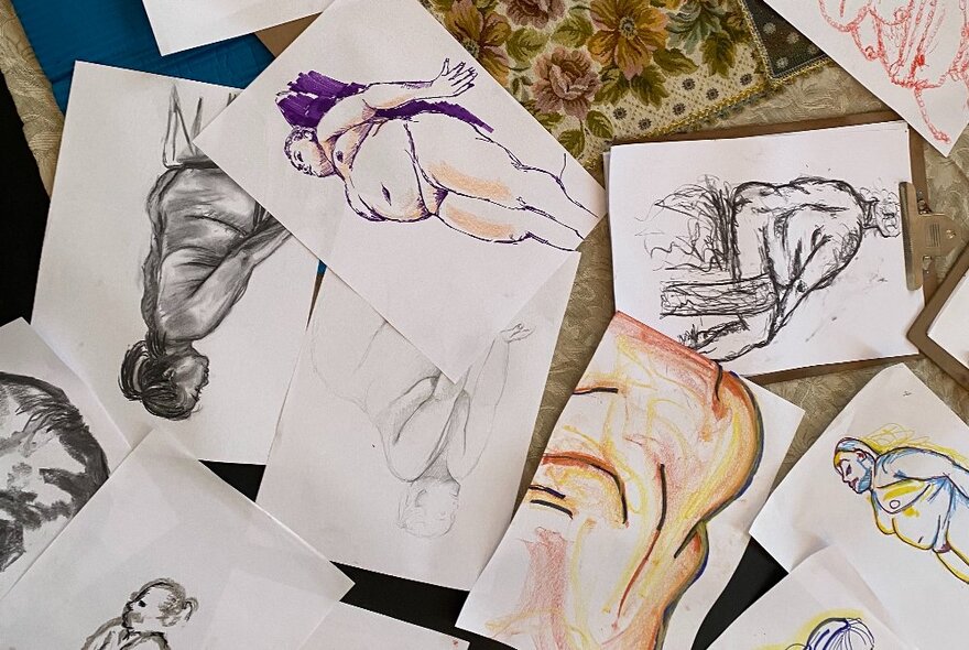 A selection of life drawing sketches on paper, arranged on a table.