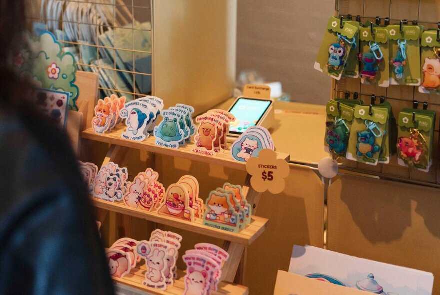 A stall at the Bloom Art Market displaying small cute cards on wooden shelves.