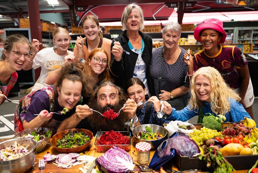 A group of people gathered around a table with vegetables of all kinds, Costa the gardener in the middle. 