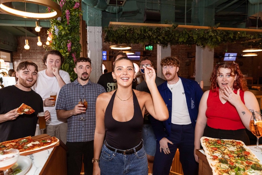 A group of friends playing darts at Oche Melbourne, with platters of food on the tables near them.