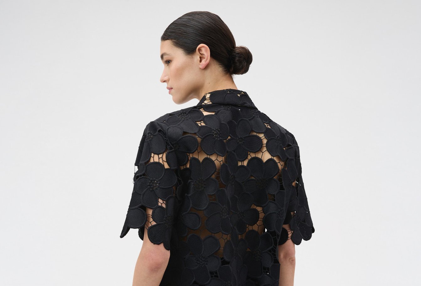 A model posing from the back with a sheer floral black lace tshirt.