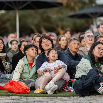 Families sitting on rugs watching movies on a big screen/