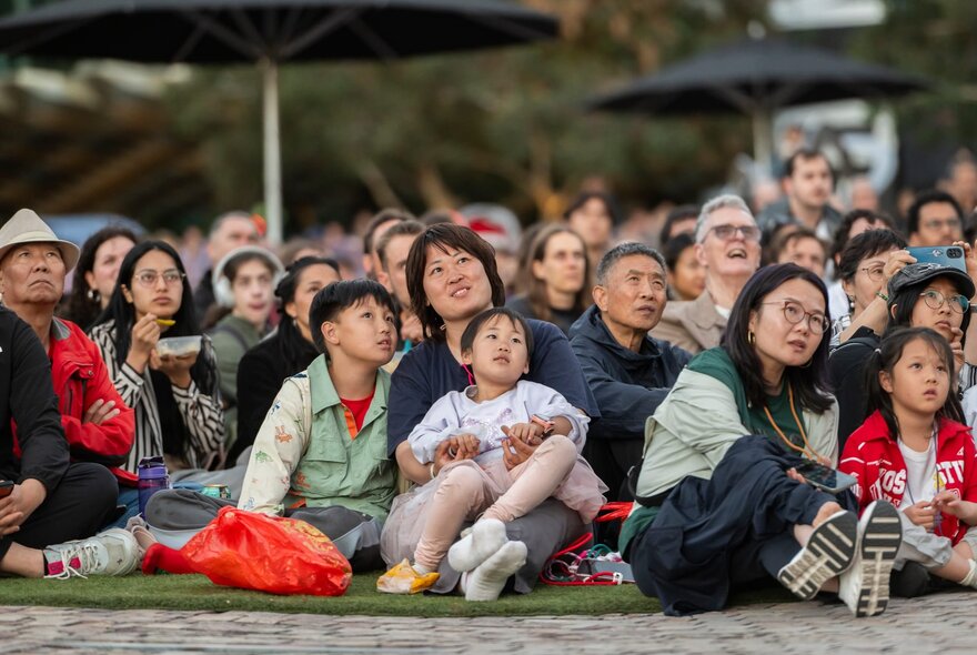 Families sitting on rugs watching movies on a big screen/