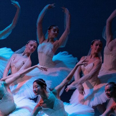 Pre-professional ballet dancers in various poses, wearing white swan-like tutus.