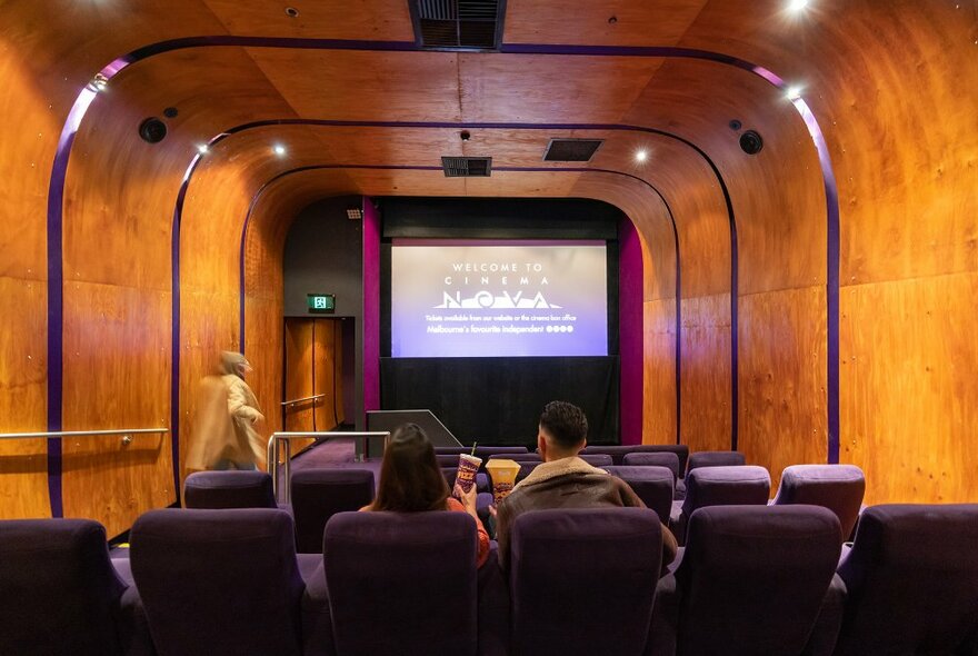 A couple sharing drinks and popcorn in a retro timber walled cinema.