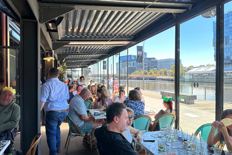 People seated at outdoor tables looking at a river promenade. 