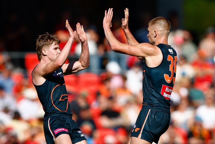 Two GWS Giants players slap hands in the air during a match. 
