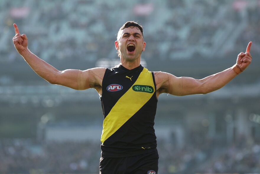 A Richmond AFL football player celebrating  with his arms raised above him, on the field during a match.