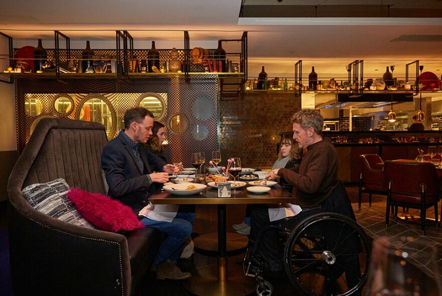 Four people eating at a restaurant, two are sitting in wheelchairs.