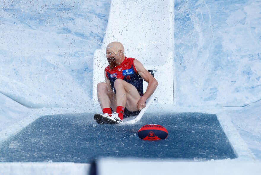 Melbourne AFL football player sliding down an icy slide as part of the pre-match Big Freeze activities.