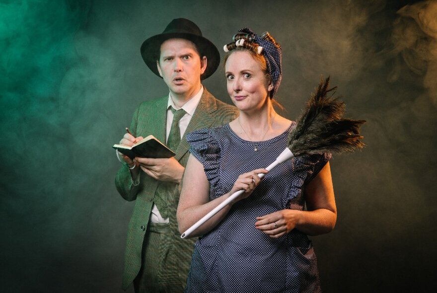 Two members of a play based on Agatha Christie-style whodunnits, wearing 1930s costumes, the woman holding a feather duster. 