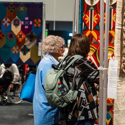 Visitors admiring handmade textile art and quilts at a craft and quilting exhibition.