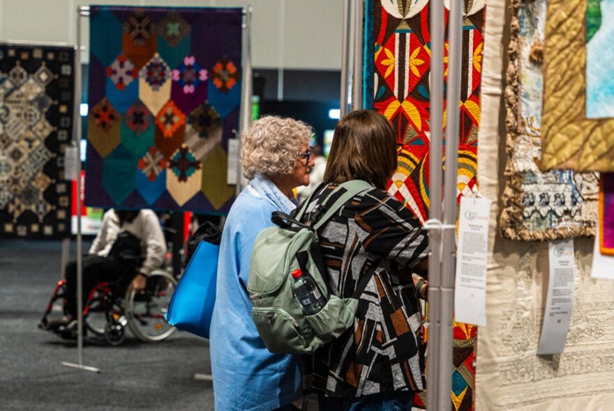 Visitors admiring handmade textile art and quilts at a craft and quilting exhibition.