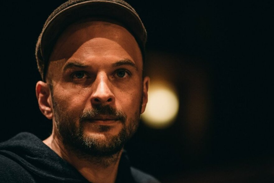 German composer and musician, Nils Frahm, wearing a brown peaked cap and hooded jumper.