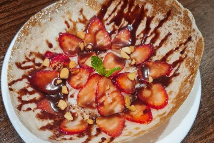 A string hopper with sliced strawberries and chocolate sauce on a plate.