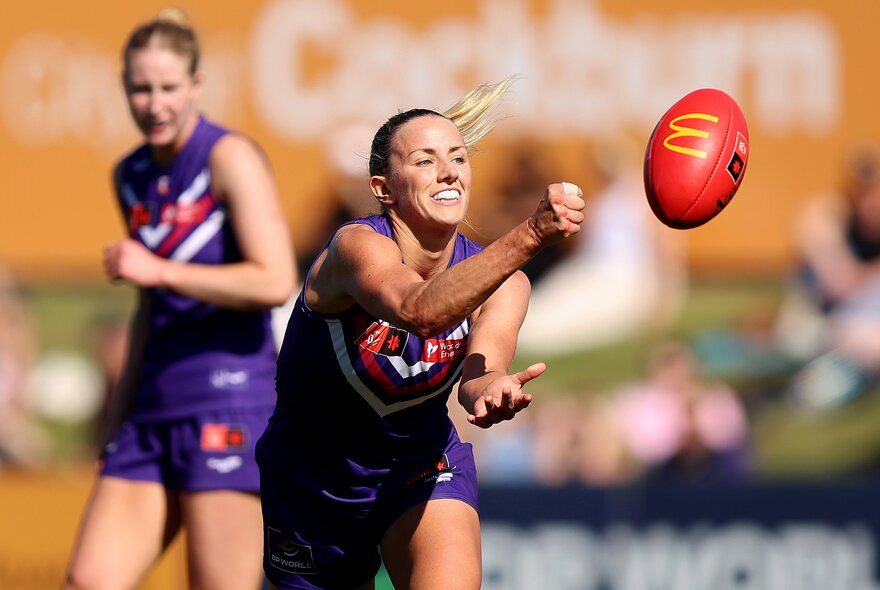 A Fremantle AFLW player handpasses during play, another player watching on. 