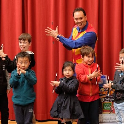 Comedian Tim Credible showing a magic trick to a group of children in front of a red curtain.
