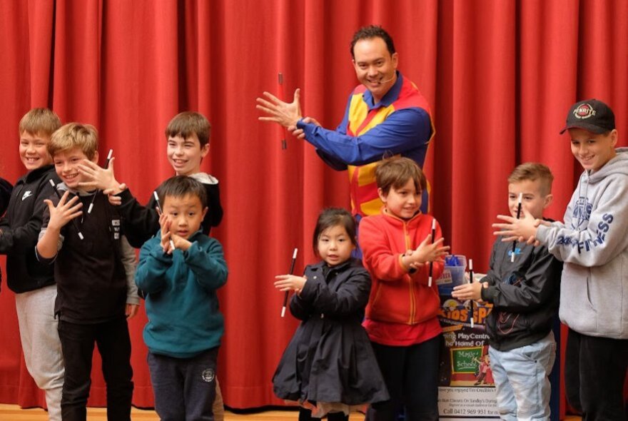 Comedian Tim Credible showing a magic trick to a group of children in front of a red curtain.
