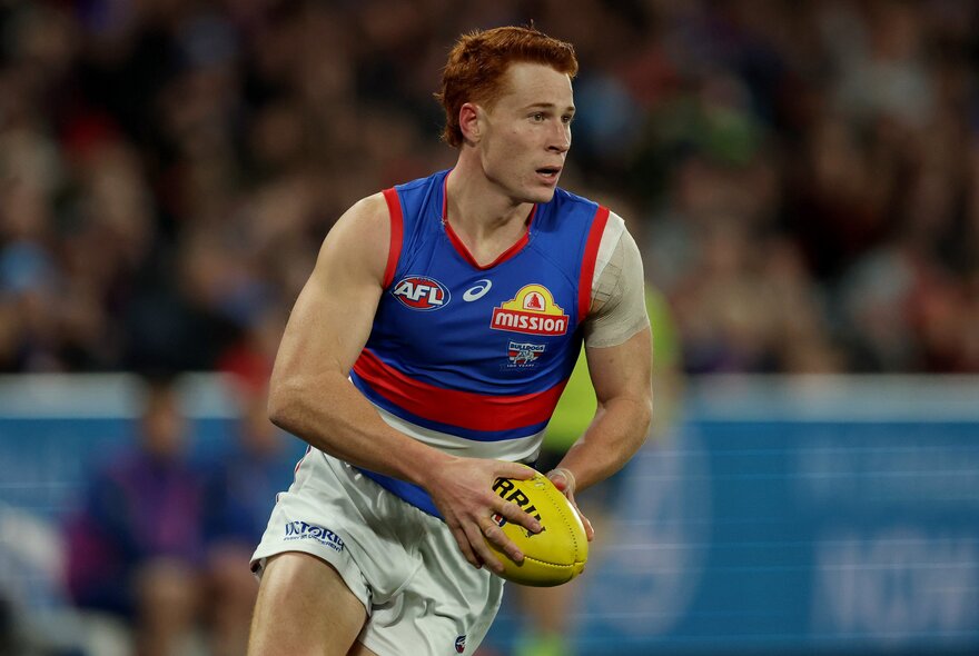 A Western Bulldog AFL football player running and holding the yellow footy on the field during a match.